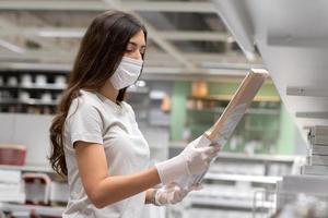 mujer con máscara protectora seleccionando el hogar para mudarse a casa o decorar una nueva habitación. nuevas compras normales durante la pandemia del coronavirus. foto