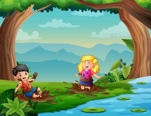 Two children have fun playing in the mud near the river
