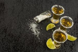 Gold tequila with lime on black background, top view photo