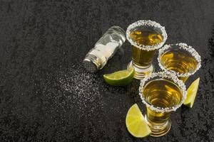 chupitos de tequila con lima y sal en mesa negra foto