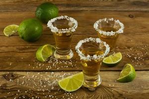 tres chupitos de tequila con limón y sal en el fondo de madera foto