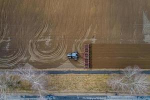 vista superior aérea de un tractor, cosechadora arando tierras agrícolas en primavera