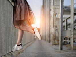 teen girl's legs in white sneakers on the bridge at sunset photo