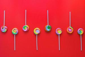 Creative flat lay of Rows of alternating colorful lollipops on a red background photo