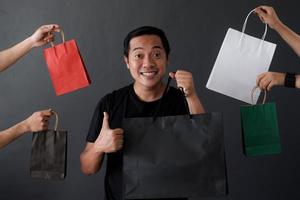 Shopaholic man surrounded by many hands holding shopping bags photo