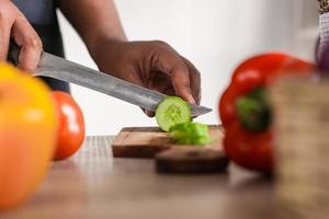 Side view Chef hold knife in hand and cut cucumber on cutting board in modern society popular concept photo