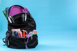 A school bag with school supplies for back to school concept with copy space on blue background photo