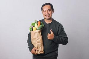 Asian man holding grocery shopping bag with vegetables with thumbs up gesture for healthy lifestyle concept photo