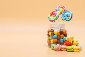 Assorted sweets in a jar and french macaroons cake on cream colored background with copy space