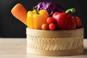 Assorted fresh vegetables in basket on wooden table photo