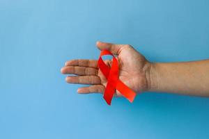 World Aids Day and World Diabetes Day with male hands holding red AIDS awareness ribbon isolated on blue background. Healthcare and medicine concept. photo