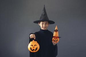 Cute Asian boy celebrating Halloween by wearing witch costume and holding Halloween decoration accessories photo
