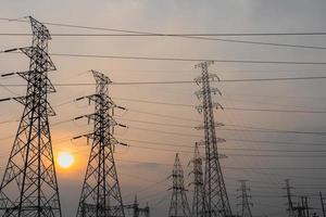Photo of high-voltage steel poles at a power plant in the evening with the setting sun