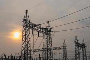Photo of high-voltage steel poles at a power plant in the evening with the setting sun