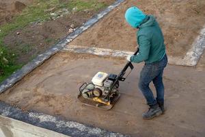 a worker with a vibrating tamping machine rams the ground photo