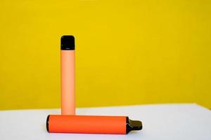 two disposable e-cigarettes on a yellow background. The concept of modern smoking, vaping and nicotine. Top view photo