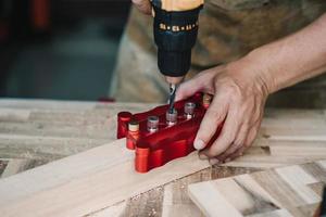 carpenter use drill bit and centering dowel jig or pocket hole jig tool to make strong joints on wooden plate at workshop. woodworking concept.selective focus. photo