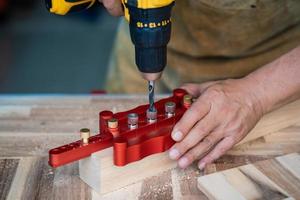 el carpintero usa una broca y una plantilla de espiga de centrado o una herramienta de plantilla de agujeros de bolsillo para hacer uniones fuertes en una placa de madera. concepto de carpintería enfoque selectivo. foto