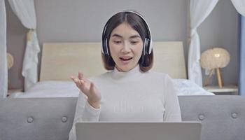 mujer que tiene una llamada web en la computadora portátil en casa, hablando a la cámara mientras se sienta en el sofá en la sala de estar. video conferencia. foto