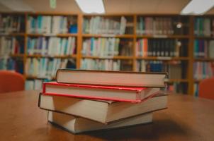 Stack of books on table and blurred bookshelf in the library room, education background. photo