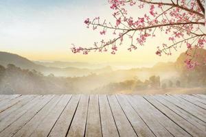 mesa de madera superior vacía y flor de sakura con niebla y fondo de luz matutina.