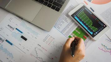 Businesswoman analyze business report graph and finance chart using smartphone and computer laptop at corporate office. photo