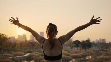 mujer joven brazos extendidos y de pie en la ciudad al atardecer. foto