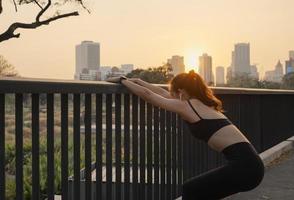 Young woman in sportswear streching on the bridge in the city at sunset. photo