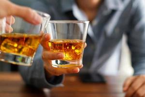 primer plano de dos hombres tintinean vasos de whisky beben bebidas alcohólicas juntos mientras están en el mostrador del bar en el pub foto