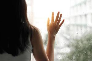 mujer triste mirando a través de la ventana de cristal con gotas de lluvia en el fondo de la ciudad foto