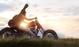 mujer guitarrista montando una motocicleta en la carretera del campo, fondo de puesta de sol foto