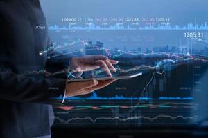 Business people checking stock market on tablet and analysing financial data on a screen with graph and candlestick chart on LED monitor virtual on the city background photo