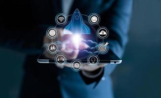 Startup concept. Businessman touching tablet and icon network connection with rocket flying out of screen on dark background photo