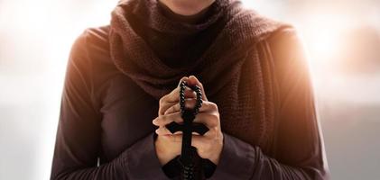 Christian Religion concept. Woman hands praying with rosary and wooden cross. Bless god helping catholic on soft background. photo