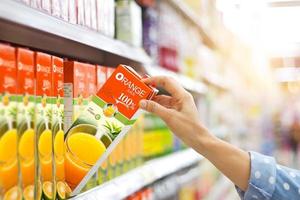 mano de mujer eligiendo comprar jugo de naranja en los estantes del supermercado foto