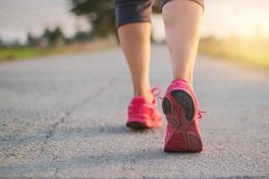cerrar la zapatilla de deporte de los pies de la corredora de la mujer atleta en la carretera rural mientras se ejecuta el ejercicio en el fondo de la puesta de sol
