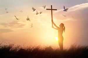 Woman praying with cross and flying bird in nature sunset background, hope concept photo