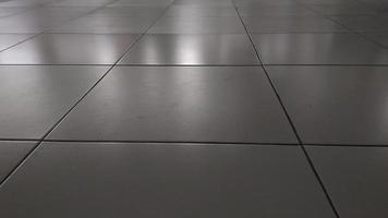 White ceramic tile floor in dim light room with soft light and shadow from outside of the building