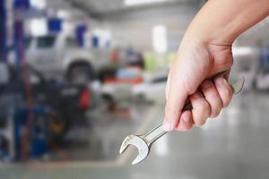 técnico sosteniendo una llave con fondo de centro de servicio de reparación de automóviles foto