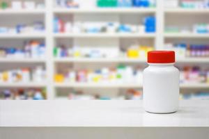 Blank white medicine bottle on counter with blur shelves of drug in the pharmacy drugstore