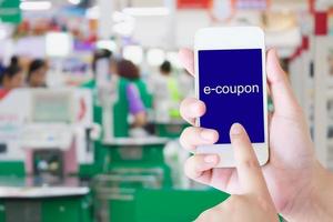 Hand holding mobile phone at supermarket checkout background, e coupon concept photo