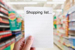 papel de lista de compras de mano con fondo de desenfoque de pasillo de supermercado
