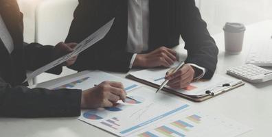 Business man holding a pen and analysis documents on office table with laptop computer and graph financial diagram working in the background. photo