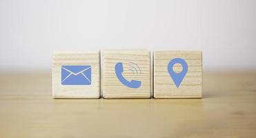 la ubicación del teléfono con letras azules y los iconos de dirección imprimen la pantalla en un bloque de cubo de madera para el concepto de contacto de servicio al cliente. foto