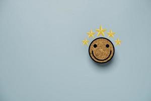 cara sonriente y pantalla amarilla de cinco estrellas impresas en un bloque de madera circular para una mentalidad positiva y un concepto de evaluación del cliente. foto