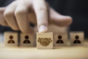 Hand putting hand shaking which print screen on wooden cube block  in front of human icon for business deal and agreement concept. photo