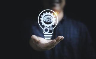 Businessman holding virtual lightbulb with mechanical gear and brain for creative thinking idea and innovation concept. photo