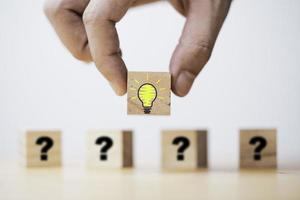 Hand putting lightbulb on wooden cube block in front of question mark for question and answer concept. photo