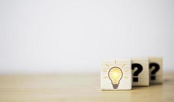 Drawing glowing lightbulb in front of question mark which print on wooden cube block for question answer and problem solving solution concept. photo