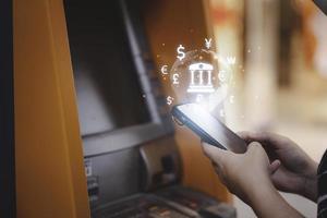 Woman hand using smartphone for transfer money between mobile phone and Automatic Teller Machine or ATM , Financial technology concept. photo